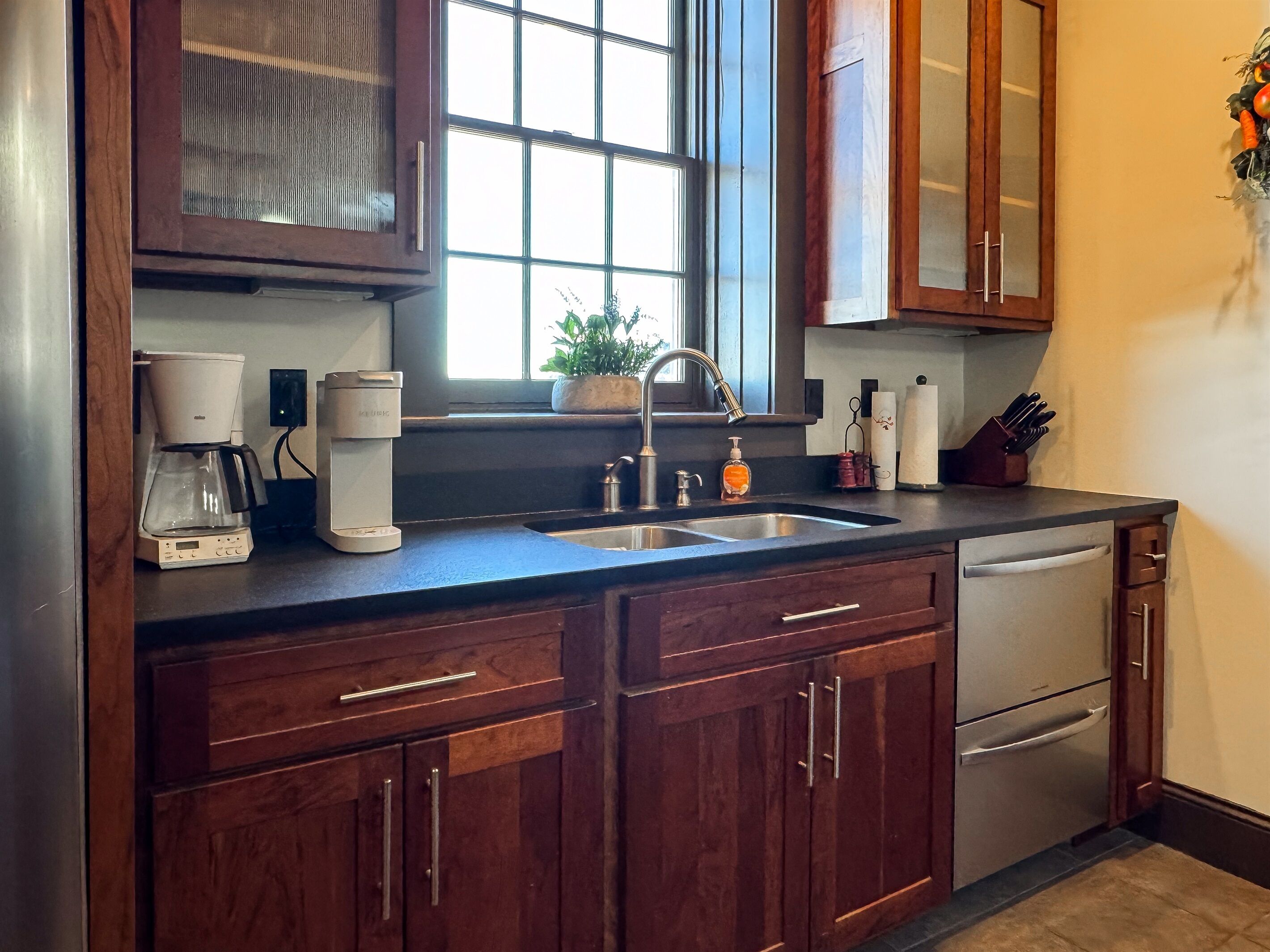 A kitchen with wooden cabinets, a coffee maker, a sink, and a window with a view.