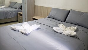 Habitació d'hotel amb dos llits, cada un amb roba de llit gris i tovalloles blanques disposades en un dibuix floral.
