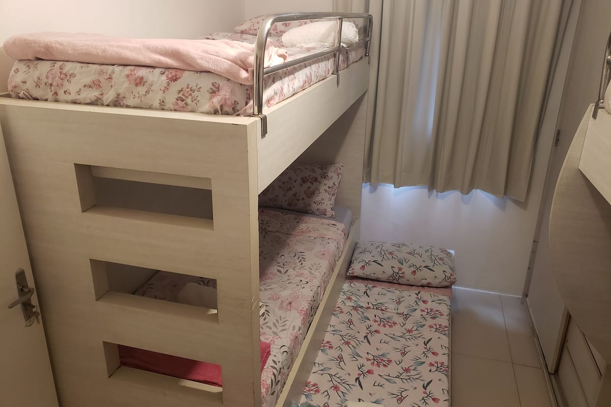A bunk bed with a wooden ladder, a small desk, and a window with curtains.