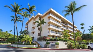 A multi-story hotel with balconies, palm trees, and a clear blue sky.