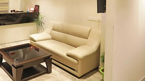 A beige sofa, a glass coffee table, and a small plant in a living room. - Hotel GoodLuck House Near Delhi Airport (New Delhi)