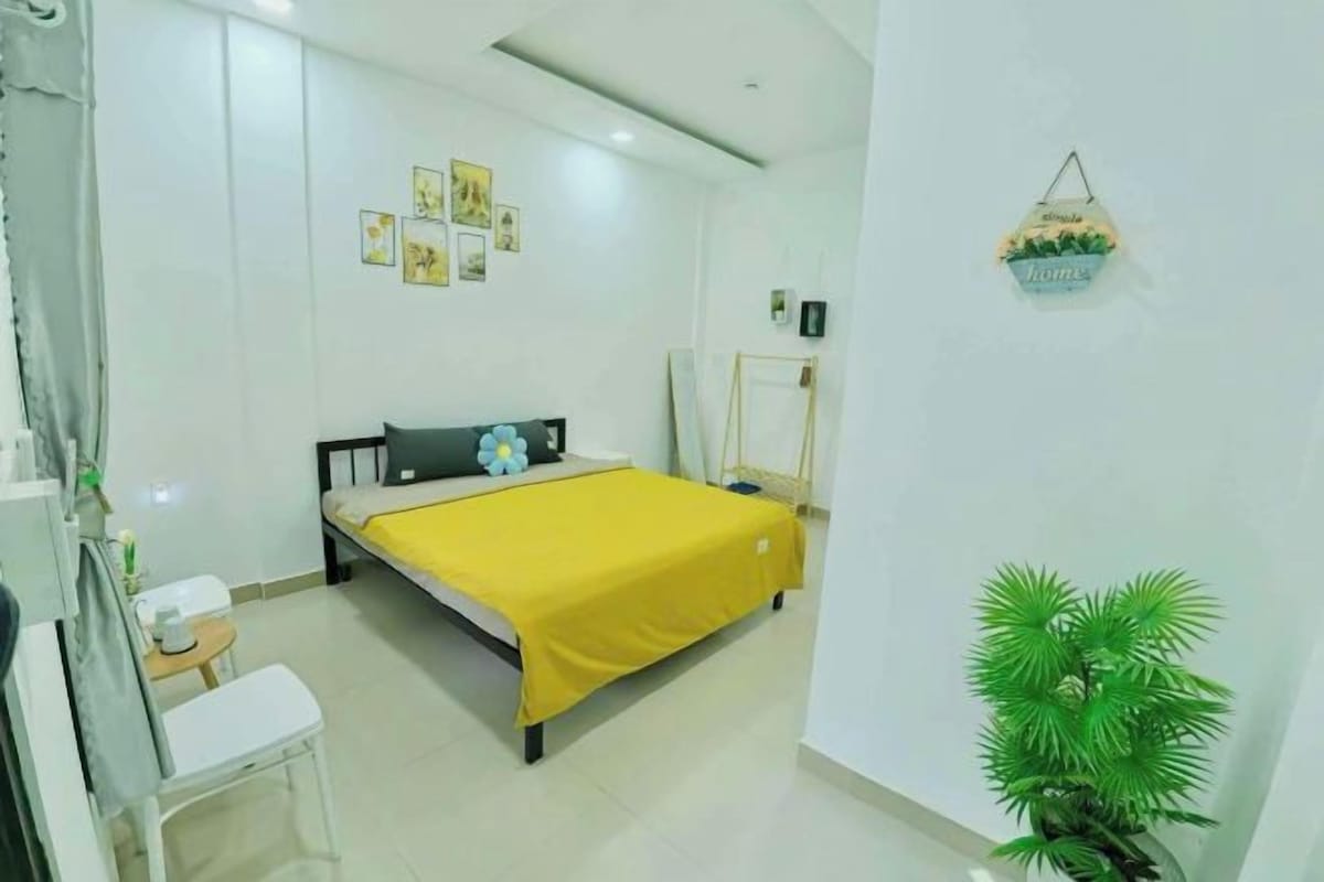 Un dormitorio con cama, una mesita, una silla, una planta en maceta y decoración en la pared.