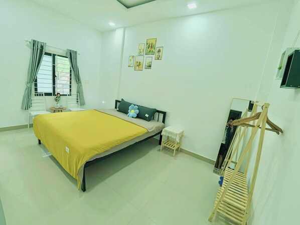 A clean, well-lit bedroom with a bed, bedside table, and a small stool.