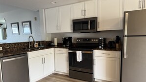 Una cocina moderna con armarios blancos, un refrigerador de acero inoxidable, un microondas, una estufa y un lavavajillas.