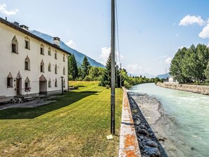 Un bâtiment à la façade symétrique, une rivière au premier plan et un paysage montagneux en arrière-plan.