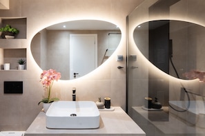 A modern bathroom with a large oval mirror, a white sink, and a shower area. - Loft Suite In Syntagma |Metro |Best Location (Athens)