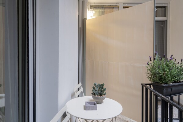A small round table with a potted plant and a box on it, a white chair, and a view of a building through a glass door. - Loft Suite In Syntagma |Metro |Best Location (Athens)
