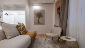 A modern living room with a sofa, a chair, a small round table, and a painting on the wall. - Loft Suite In Syntagma By Metro | Best Location (Athens)