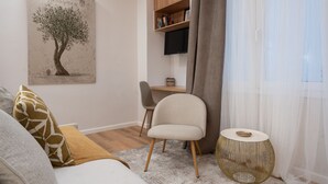 A modern living room with a sofa, a chair, a small table, a bookshelf, and a painting of a tree. - Loft Suite In Syntagma By Metro | Best Location (Athens)