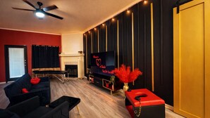 A modern living room with a fireplace, a television, and a red ottoman. - Luxury Couples Hideaway | King Bed • Jacuzzi Spa • Private Retreat (Killeen)