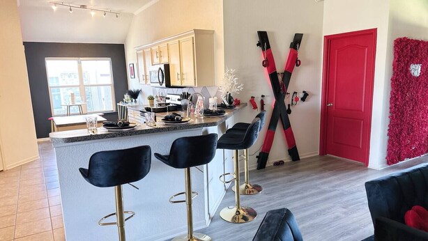 A modern kitchen with a central island, bar stools, and a red door. - Luxury Couples Hideaway | King Bed • Jacuzzi Spa • Private Retreat (Killeen)