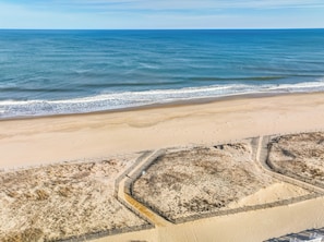 Una playa con arena dorada y un mar azul cristalino. Se observan dos zonas delimitadas por vallas con vegetación.