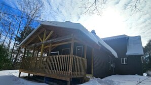 Une cabane en bois dotée d’une terrasse, entourée de neige et d’arbres.