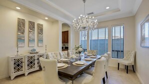 Une salle à manger avec une grande table dressée pour six personnes, entourée de chaises blanches à revêtement en tissu, d’un lustre et d’œuvres d’art accrochées aux murs.