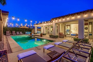 A pool area with lounge chairs and string lights.