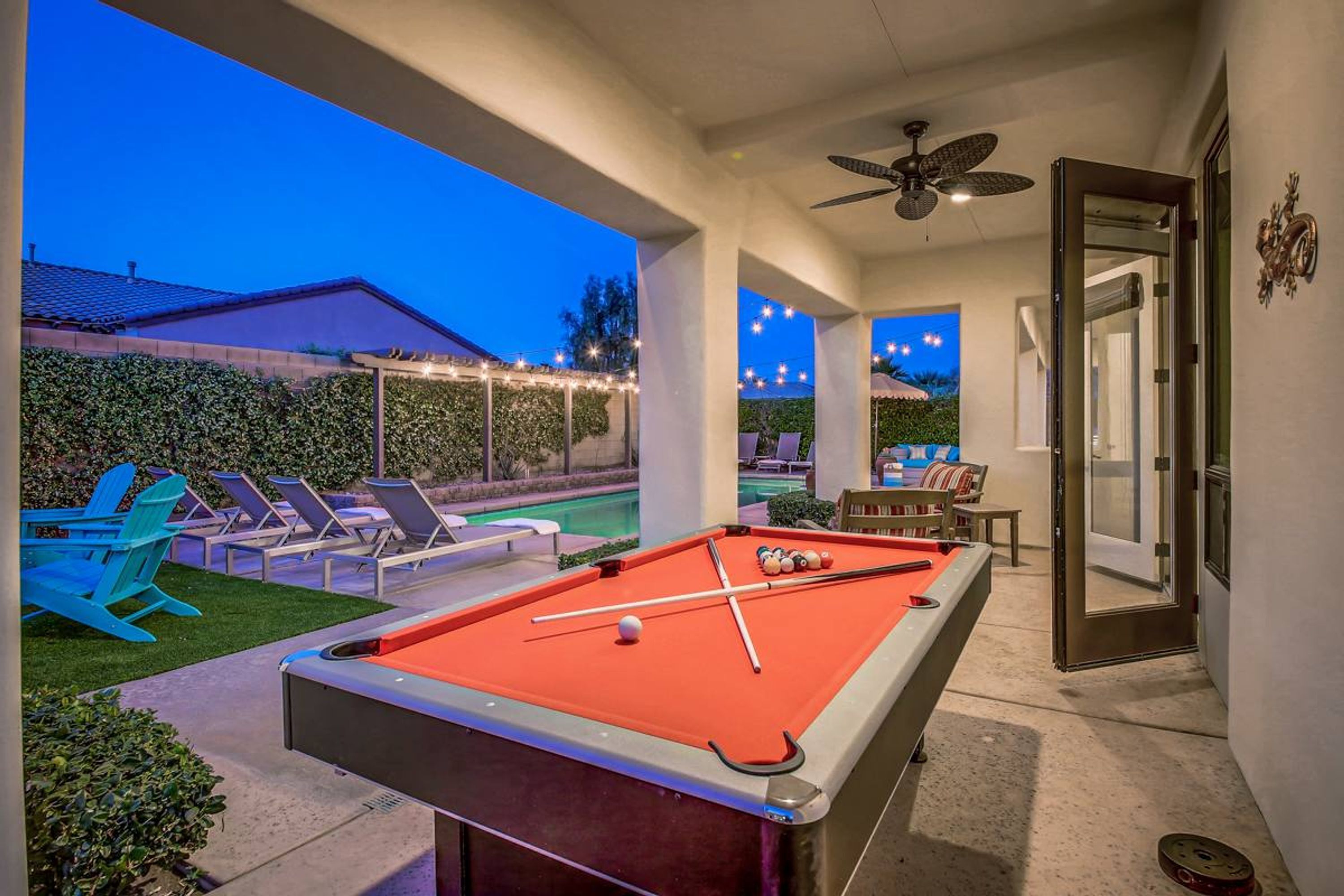 An indoor pool area with a pool table, lounge chairs, and a ceiling fan.
