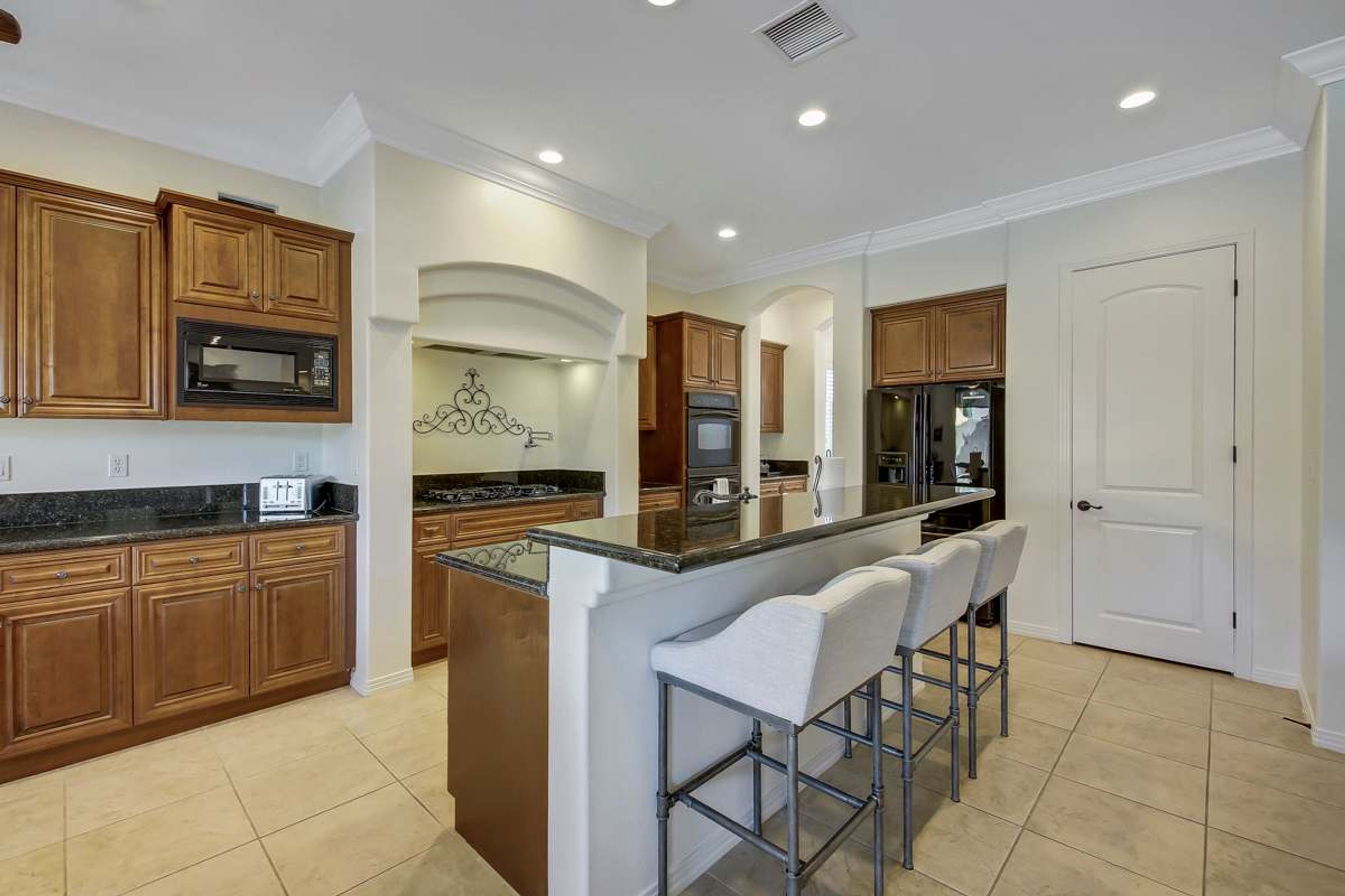 A kitchen with wooden cabinets, a central island with bar stools, a microwave, and a refrigerator.