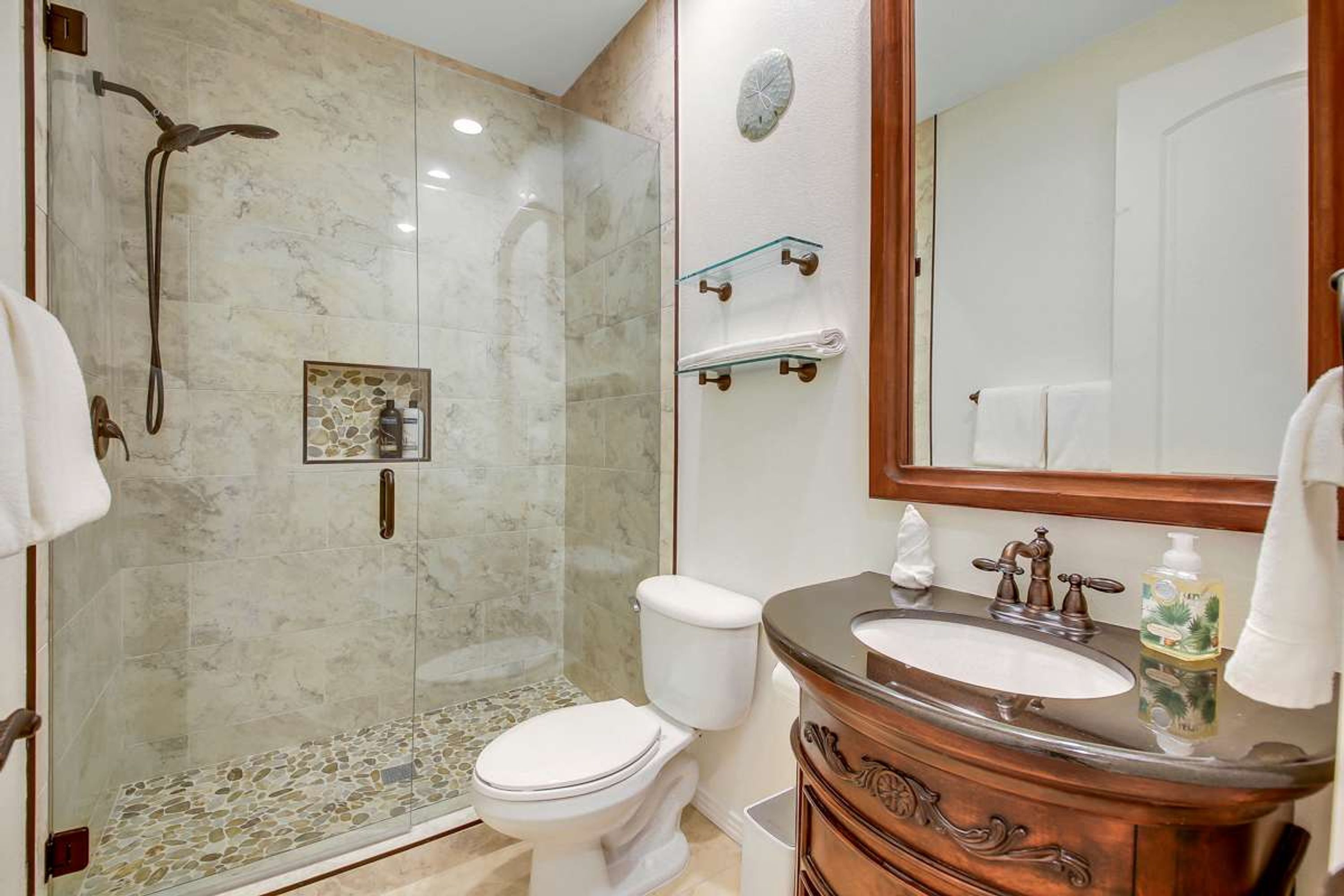 A bathroom with a glass-enclosed shower, a white toilet, a wooden vanity with a sink, and a mirror.