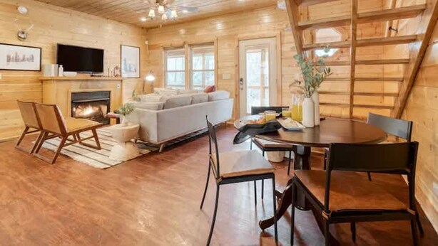 A cozy log cabin interior with a fireplace, a sofa, a dining table, and a TV.