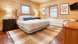 A wooden cabin bedroom with a bed, two bedside tables, a ceiling fan, and framed artwork on the walls.