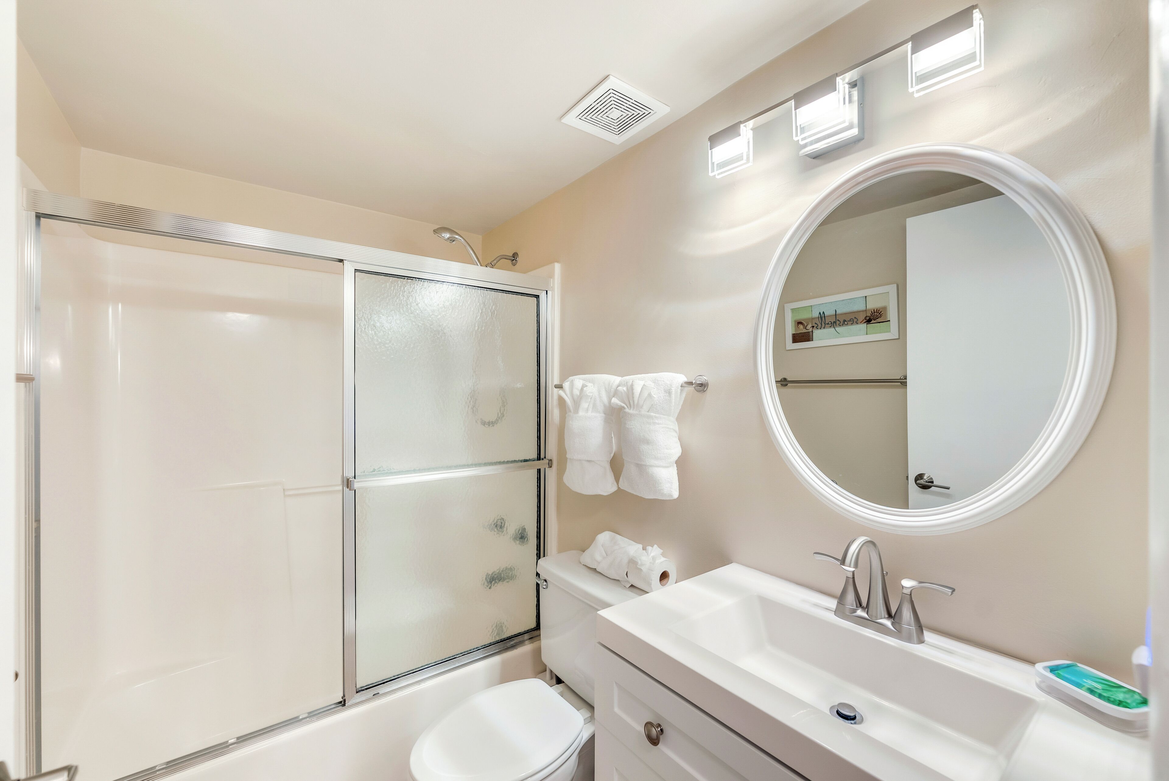 A bathroom with a glass-enclosed shower, a toilet, a sink with a mirror, and towels hanging on the wall.
