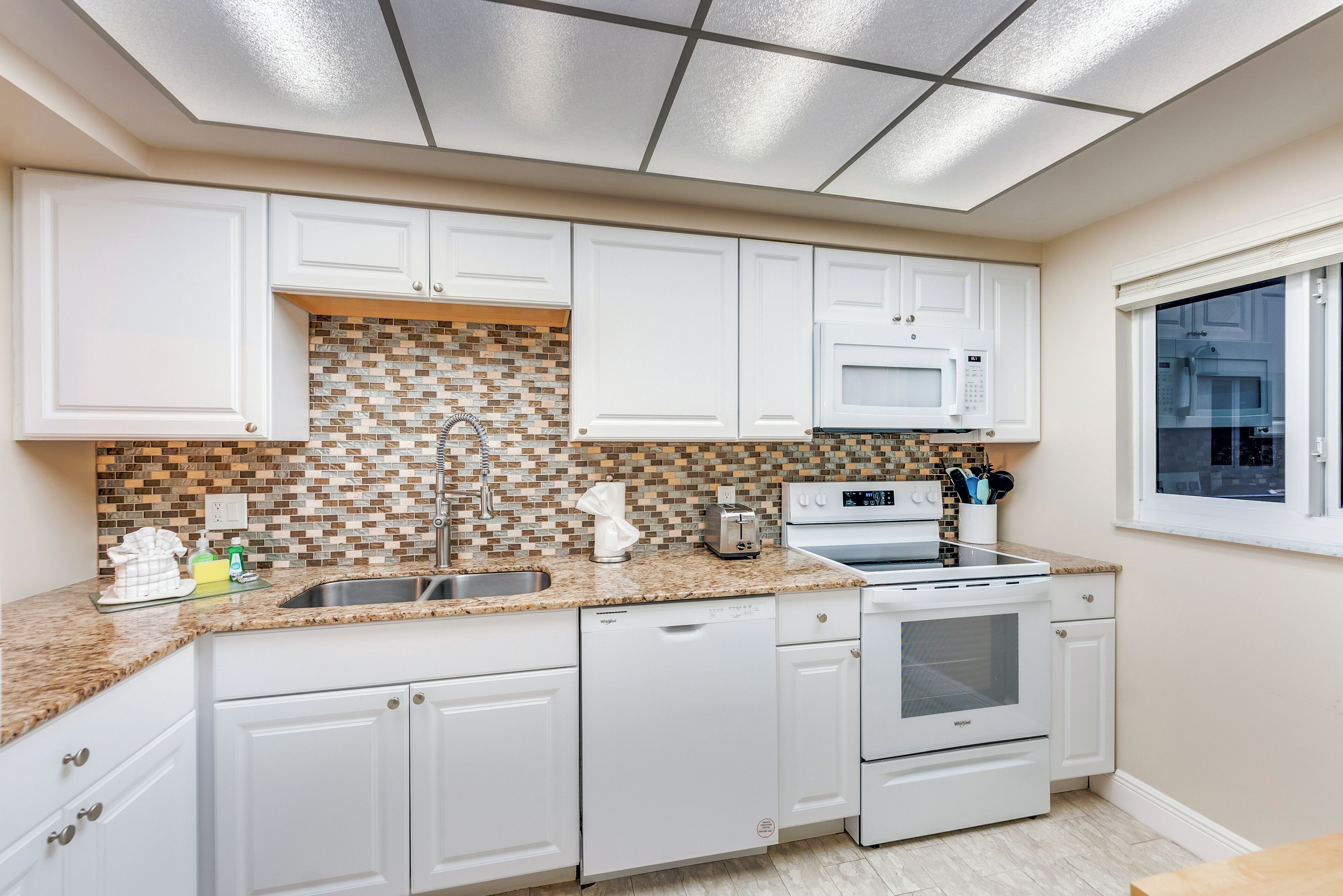 A modern kitchen with white cabinets, a tiled backsplash, a built-in microwave, and a dishwasher.