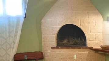 A kitchen with a brick oven, hanging light bulbs, a table with breakfast items, and a window with a curtain.
