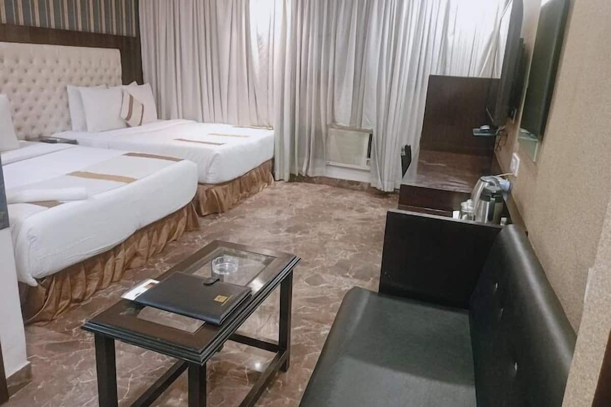 A hotel room with two beds, a glass-top table, a sofa, a TV, and a window with curtains.