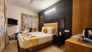 Quarto de hotel com cama, mesa de cabeceira, escrivaninha e uma secretária com chaleira.