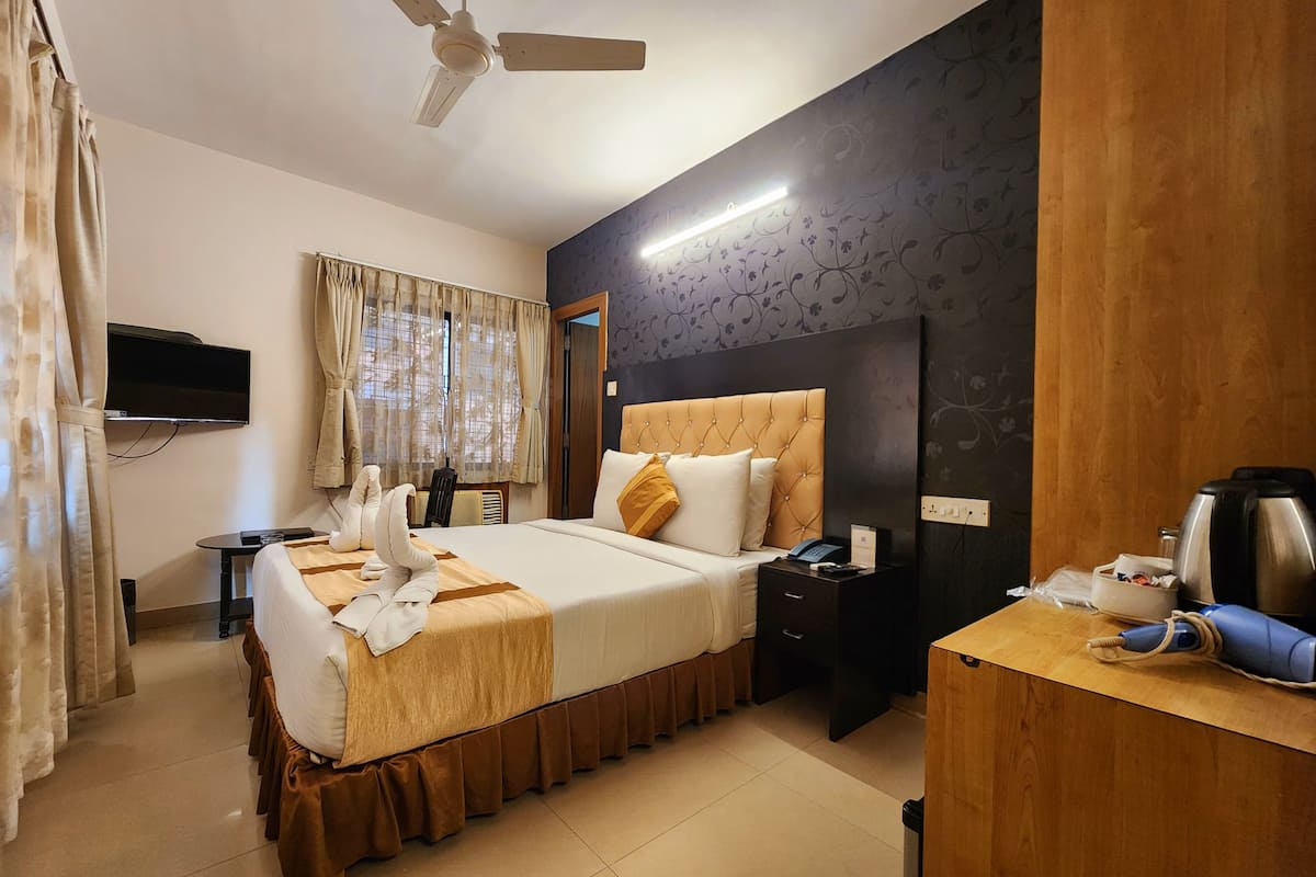 A hotel room with a bed, bedside table, nightstand, and a desk with a kettle.