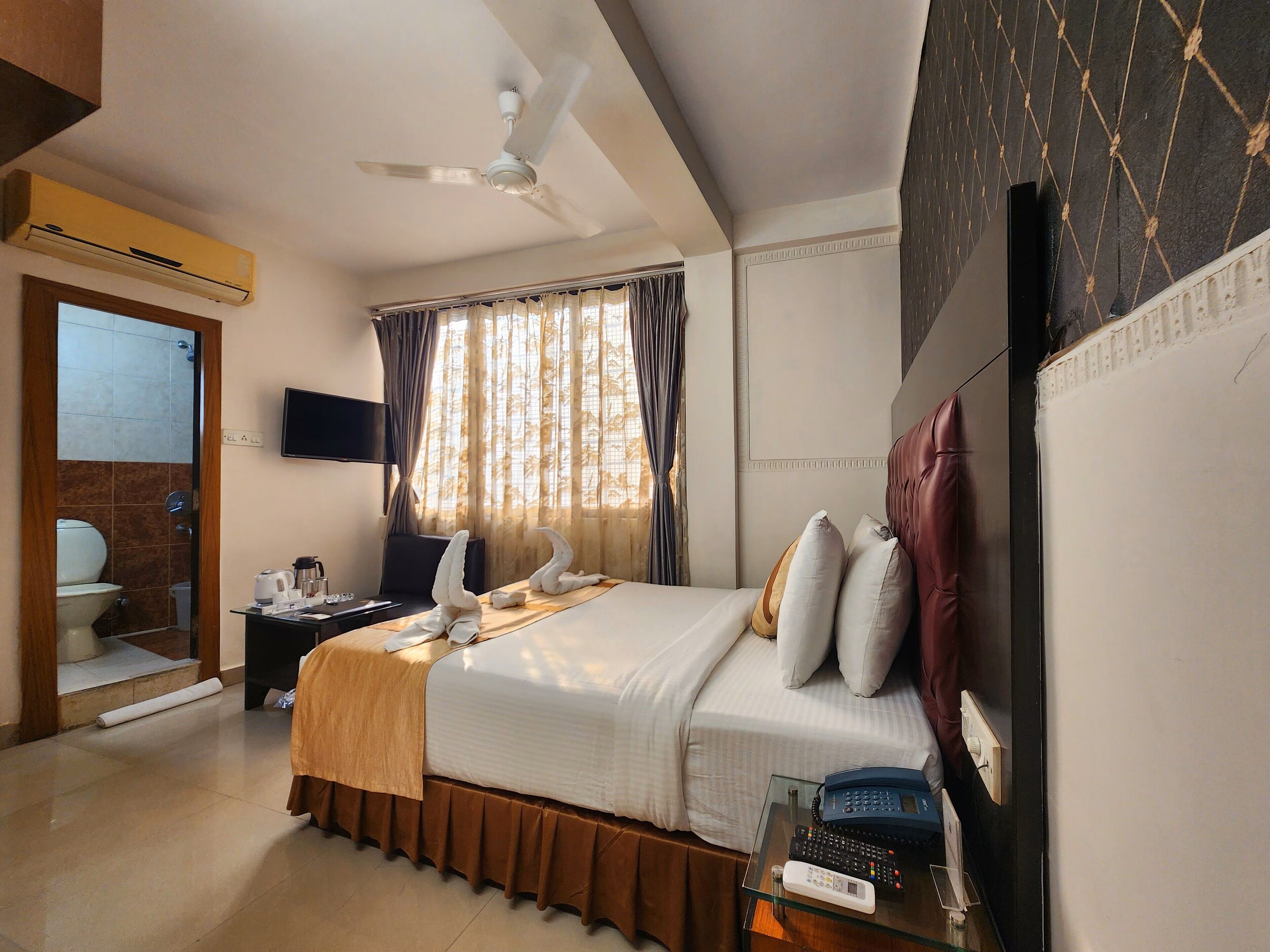 A hotel room with a bed, a desk with a telephone, a television, and a ceiling fan.