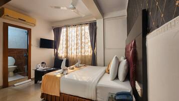A hotel room with a bed, a desk with a telephone, a television, and a ceiling fan.
