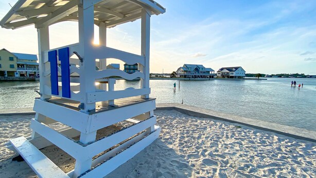 A beach with a lifeguard tower and a pier extending into the water. - Azure Horizon Beachfront Charm in Gulf Shores (Gulf Shores)