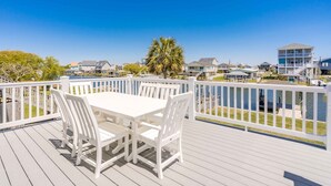A deck with a table and chairs, overlooking a marina with boats and houses. - Sunsets on Broadway - Stunning 4 BR Home - Dock & Great Outdoor Spaces (Surf City)