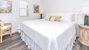 A bedroom with a large bed, a chair, a window with blinds, and two wall-mounted lamps. - Sunsets on Broadway - Stunning 4 BR Home - Dock & Great Outdoor Spaces (Surf City)