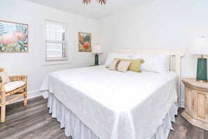 Un dormitorio con una cama grande, una silla, una ventana con persianas y dos lámparas de pared.