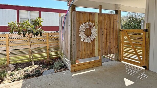 A covered outdoor area with a wooden gate, a decorative wreath, and a small tree. - Sunsets on Broadway - Stunning 4 BR Home - Dock & Great Outdoor Spaces (Surf City)