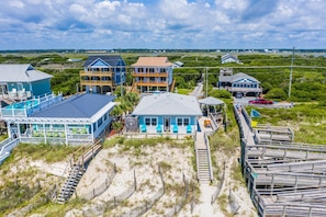 Eine Küstenimmobilie mit mehreren Gebäuden, darunter ein großes blaues Haus mit Balkon, ein kleineres blaues Haus mit Veranda und ein zweistöckiges Gebäude mit rotem Dach. Holzstege und ein Sandstrand sind ebenfalls vorhanden.