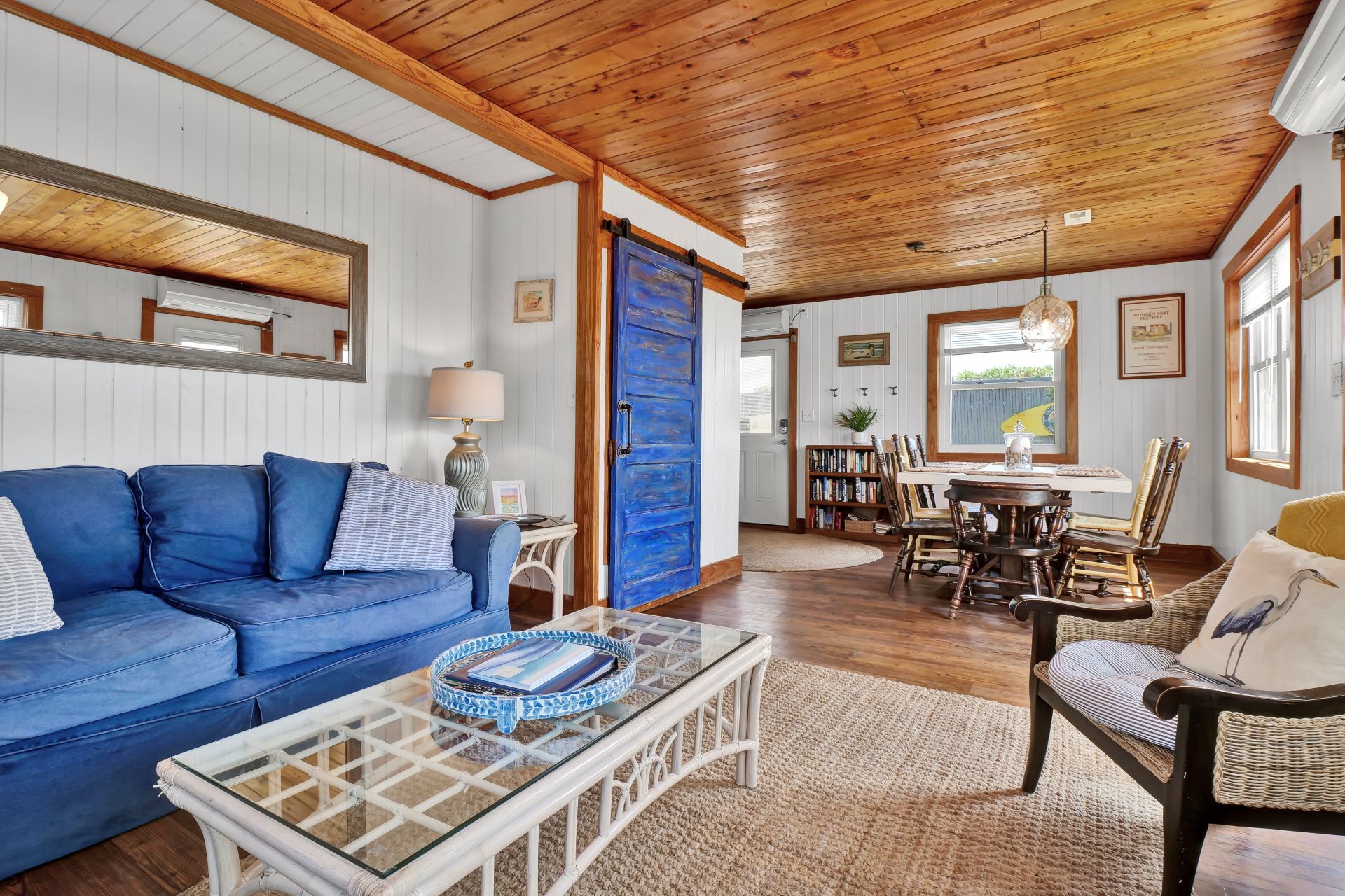 A cozy living room with a blue sofa, a glass coffee table, and a dining area with wooden chairs and a table.