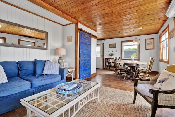 Ein gemütliches Wohnzimmer mit einem blauen Sofa, einem Glastisch und einem Essbereich mit Holzsesseln und einem Tisch.
