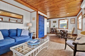 Ein gemütliches Wohnzimmer mit einem blauen Sofa, einem Glastisch und einem Essbereich mit Holzsesseln und einem Tisch.