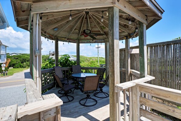 A wooden gazebo with a table and chairs, surrounded by a wooden deck.