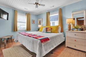 A bedroom with a bed, bedside tables, a dresser, a ceiling fan, and a window with curtains.