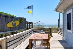 A wooden deck with a table and chairs, overlooking a beach with the ocean in the background. - Seaworthy - Dog Friendly, Updated Classic Cottage with Bonus Space! (Topsail Beach)