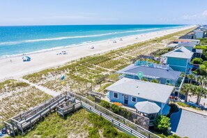 A beachfront property with a wooden boardwalk leading to a house with a blue roof, a beach in the background, and a clear sky. - Seaworthy - Dog Friendly, Updated Classic Cottage with Bonus Space! (Topsail Beach)