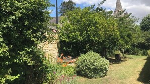 A garden with a stone wall, a lamp post, and a church steeple in the background. - Le Dorelot du lièvre, house of character (Seuilly)