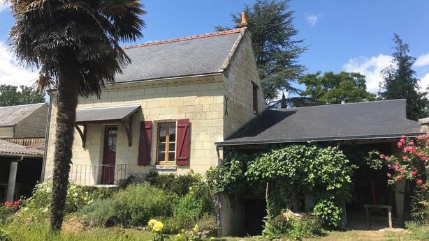 A stone house with a sloped roof, red shutters, and a garden with various plants and flowers. - Le Dorelot du lièvre, house of character (Seuilly)