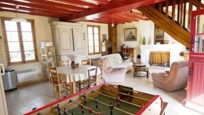 A cozy living room with a foosball table, a dining area with a round table and chairs, and a kitchen in the background. - Le Dorelot du lièvre, house of character (Seuilly)