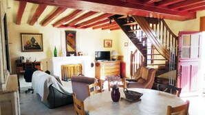A cozy living room with a sofa, a dining table, and a staircase leading to an upper level. - Le Dorelot du lièvre, house of character (Seuilly)