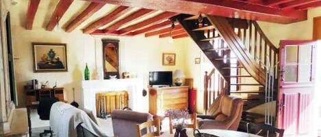 A cozy living room with a sofa, a dining table, and a staircase leading to an upper level.